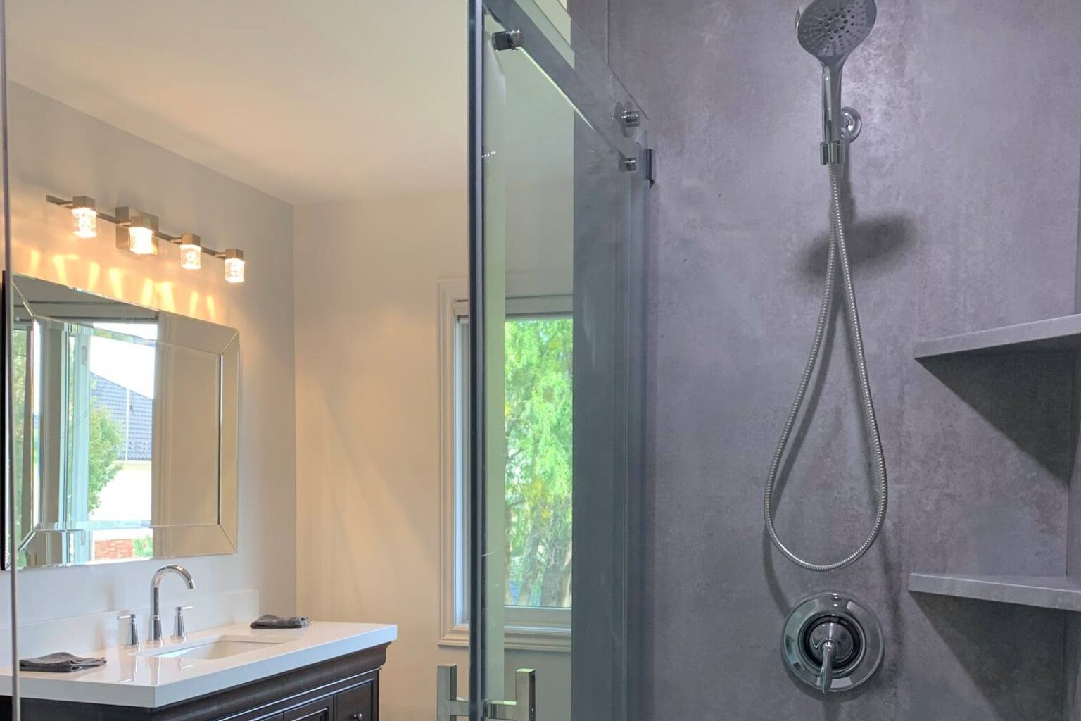 Bright bathroom with a glass walk-in shower, a handheld sprayer and a double vanity beside a window