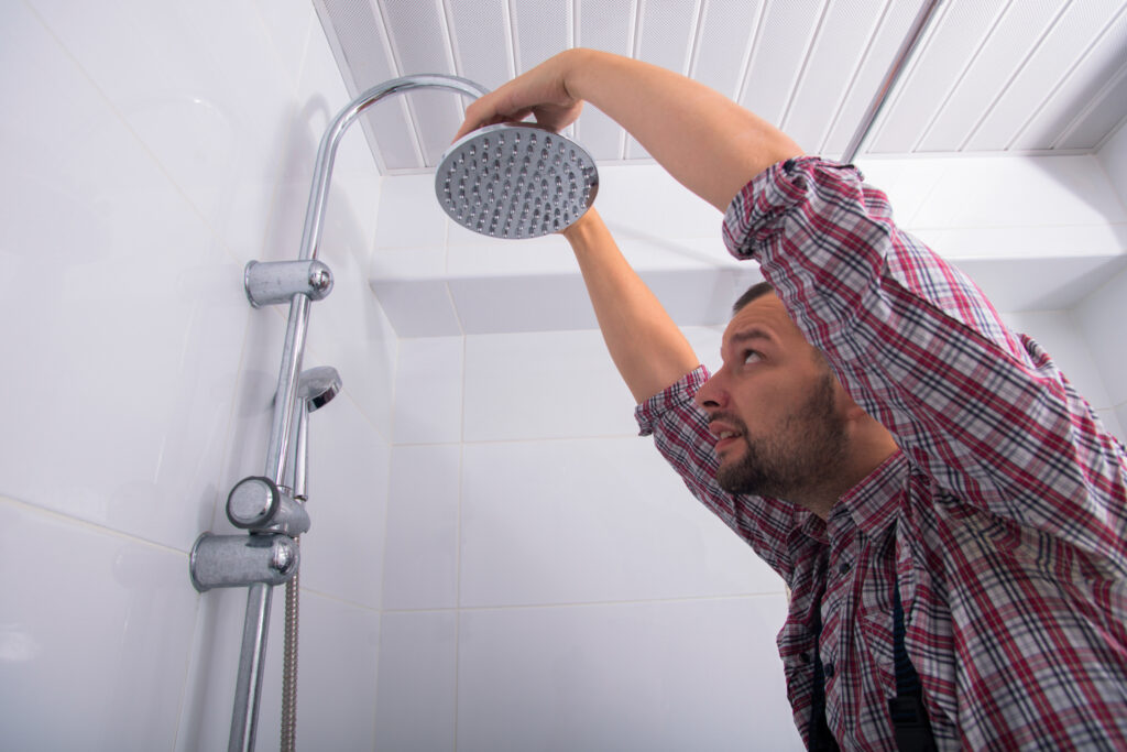 A man installs a new showerhead fixture in a shower as part of an eco-friendly bathroom conversion project. 
